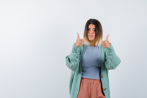 Femme en vêtements décontractés montrant deux pouces vers le haut et l'air satisfait, vue de face.