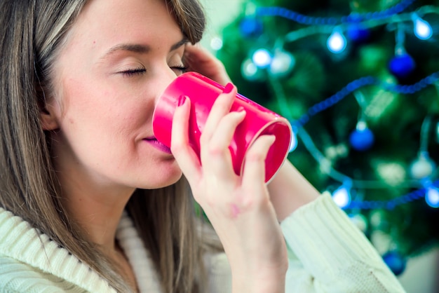 Femme en vêtements d&#39;hiver bénéficiant d&#39;une boisson chaude yeux fermés. Portrait d&#39;une jeune femme heureuse avec une tasse de chocolat chaud