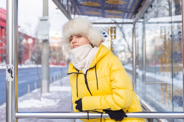 Femme en vêtements d'hiver par une journée froide en attente d'un bus à un arrêt de bus