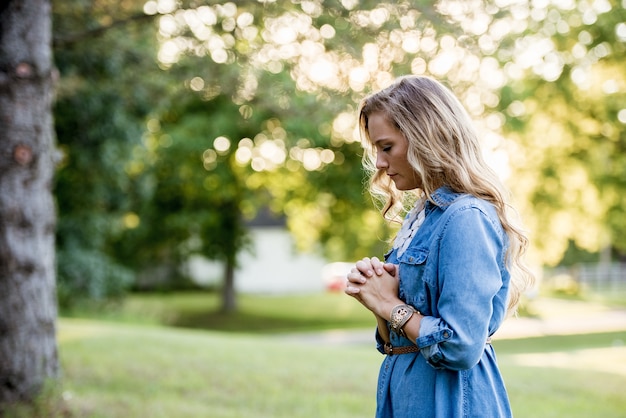 Femme vêtue d'une robe bleue et priant dans un jardin sous la lumière du soleil