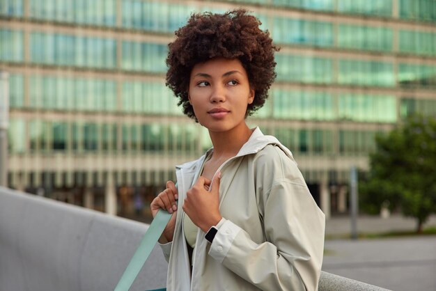 femme vêtue d'une veste porte karemat étant sur le chemin du studio de sport regarde loin pose pensivement à l'extérieur