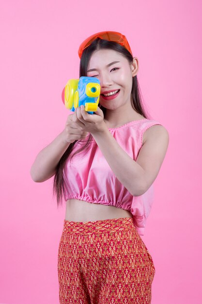 Une femme vêtue d&#39;un vêtement traditionnel thaïlandais tenant un pistolet à eau sur un fond rose.