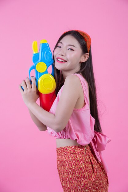 Une femme vêtue d&#39;un vêtement traditionnel thaïlandais tenant un pistolet à eau sur un fond rose.