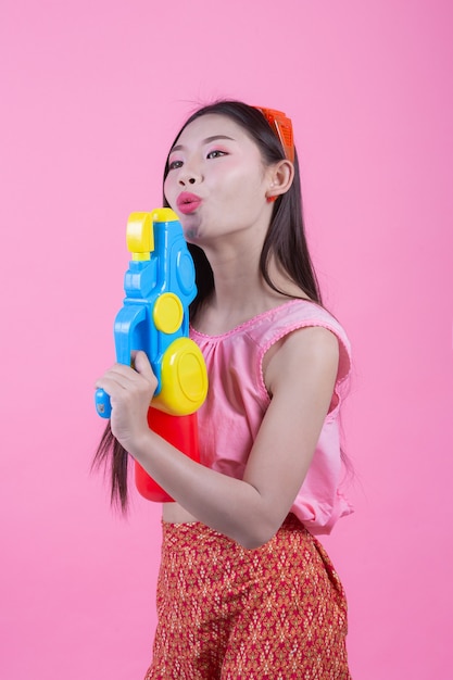 Une femme vêtue d&#39;un vêtement traditionnel thaïlandais tenant un pistolet à eau sur un fond rose.