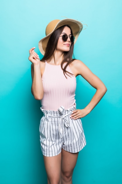 Femme de voyage d'été en chapeau et lunettes de soleil prêt pour un voyage de fête et une fête isolée sur un mur bleu. Jolie fille souriante pensant aux vacances. Ambiance d'été.