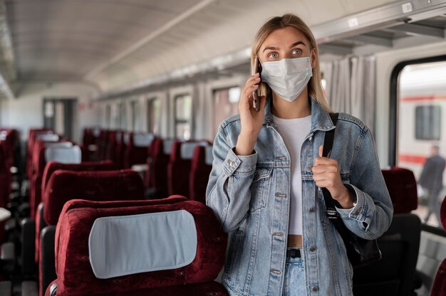 Femme voyageant en train et parlant au téléphone tout en portant un masque médical