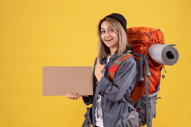 femme voyageur avec sac à dos rouge tenant un carton pointant derrière