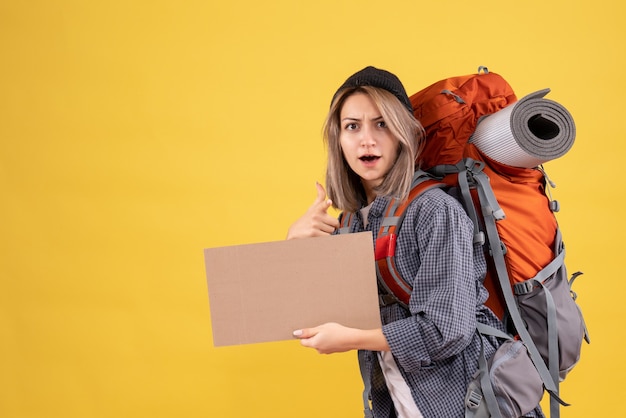 femme voyageur avec sac à dos tenant un carton pointant vers la caméra