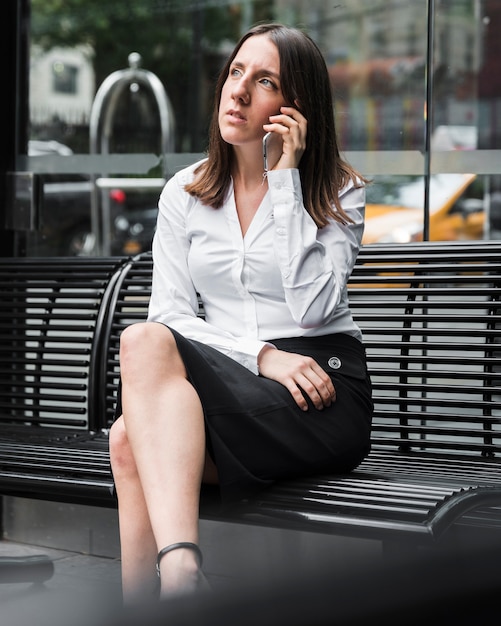 Femme vue de côté, assis sur un banc avec téléphone