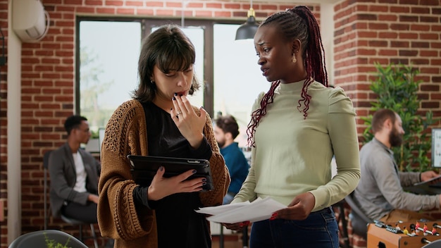 Femmes d'affaires analysant des informations sur papier et tablette numérique, travaillant en équipe pour créer une présentation de démarrage. Utilisation de tableaux de données pour planifier un projet de partenariat, rapport de recherche.