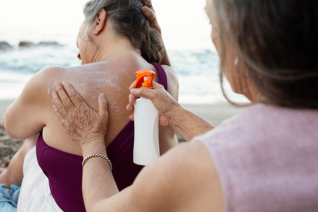 Femmes âgées appliquant un écran solaire sur le dos à la plage