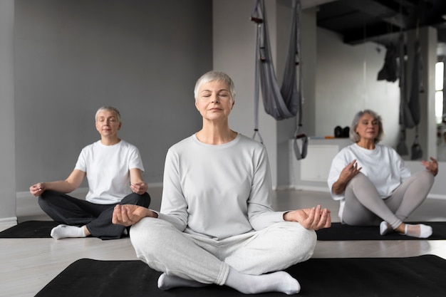 Femmes âgées faisant des exercices de yoga dans la salle de sport sur des tapis de yoga