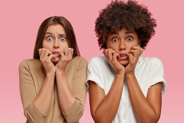 Les femmes effrayées et émotives se sentent lâches, paniquées, les yeux pleins de peur, inquiètes des dernières nouvelles, modèle contre le mur rose. Deux femmes ont peur de la phobie, expriment le choc et la peur