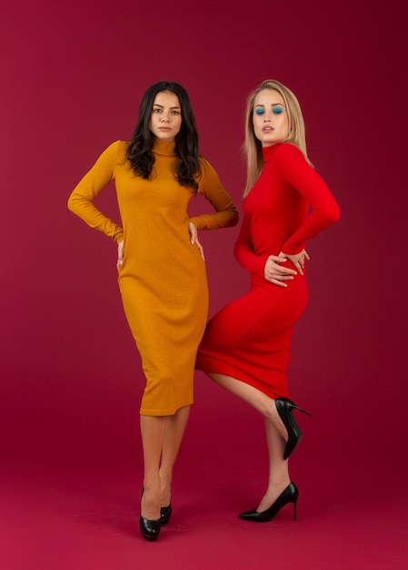 Femmes élégantes en robe tricotée de mode automne hiver jaune et rouge posant isolé sur mur rouge