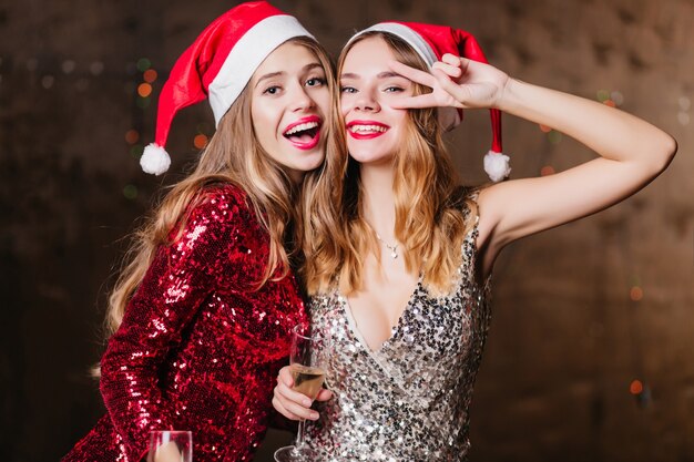 Femmes insouciantes en chapeaux de nouvel an dansant drôle et souriant, passant du temps à la fête