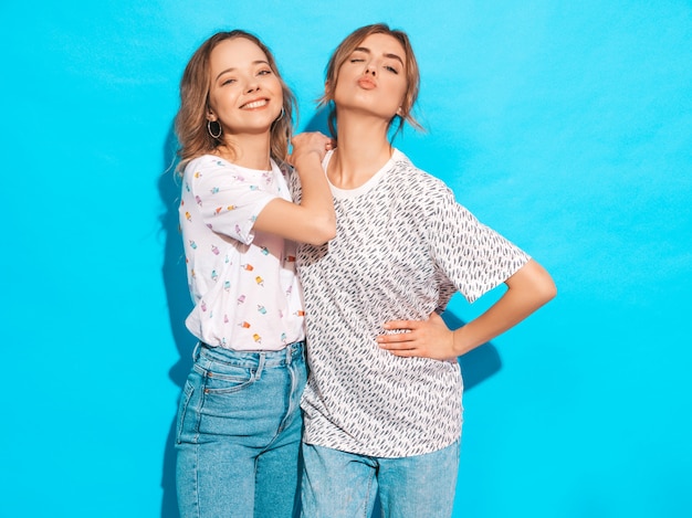 Femmes insouciantes sexy posant près du mur bleu. Modèles positifs s'amusant, clins d'œil et fait face