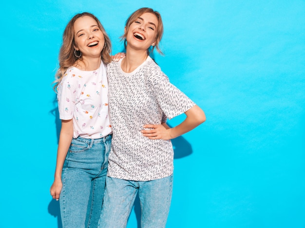 Femmes insouciantes sexy posant près du mur bleu. Modèles positifs s'amusant