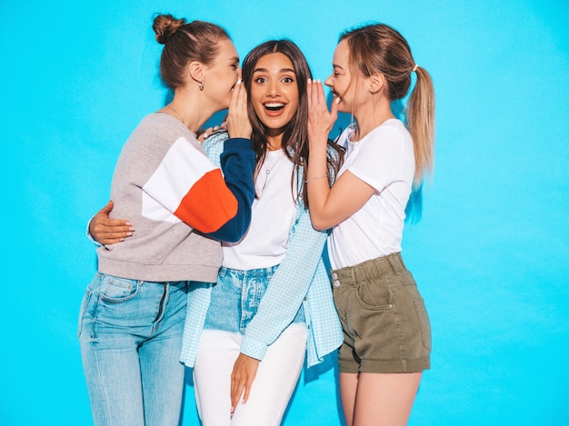 Femmes insouciantes sexy posant près du mur bleu en studio. Les mannequins positifs deviennent fous et s'amusent.