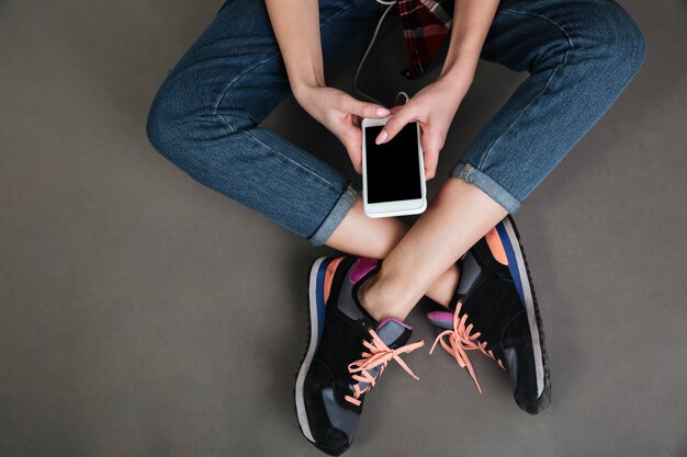 Femmes jambes croisées et mains tenant un téléphone mobile à écran blanc