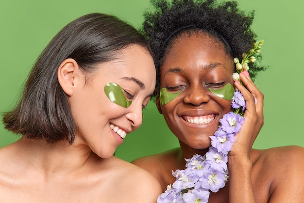 Photo gratuite les femmes métisses sourient largement appliquent des patchs d'hydrogel sous les yeux prennent soin de l'apparence tiennent la fleur