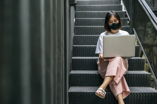 Femmes portant des masques et jouant des ordinateurs portables dans les escaliers.