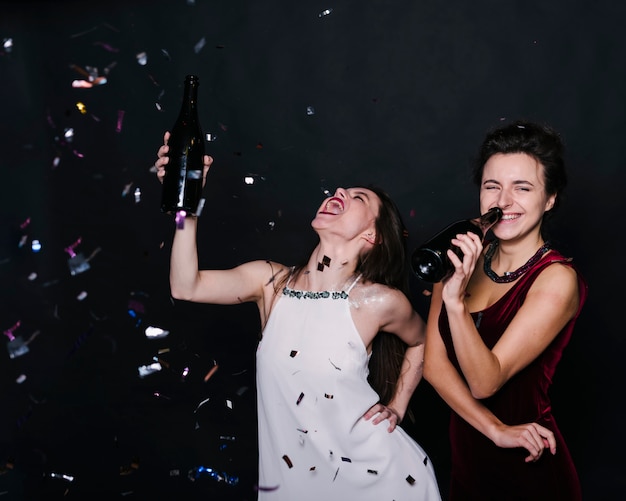 Femmes qui pleurent en robe du soir avec des bouteilles de boissons entre des confettis