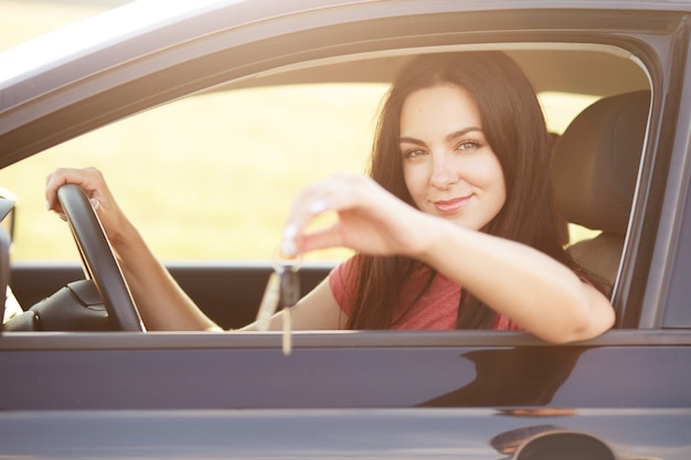 Les femmes s'assoient au siège du conducteur, gardent la main sur le volant, font de la publicité ou vendent une voiture. Belle femme brune conduit un véhicule