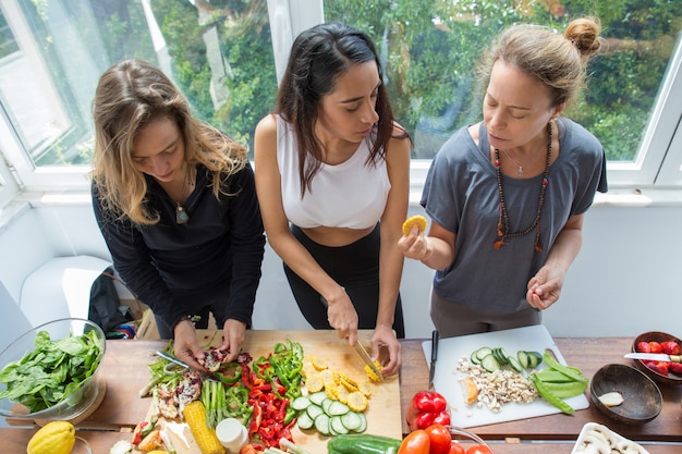 Femmes sérieuses discutant et coupant des légumes en cuisine