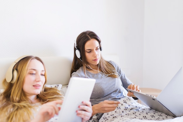 Femmes avec des technologies reposant au lit