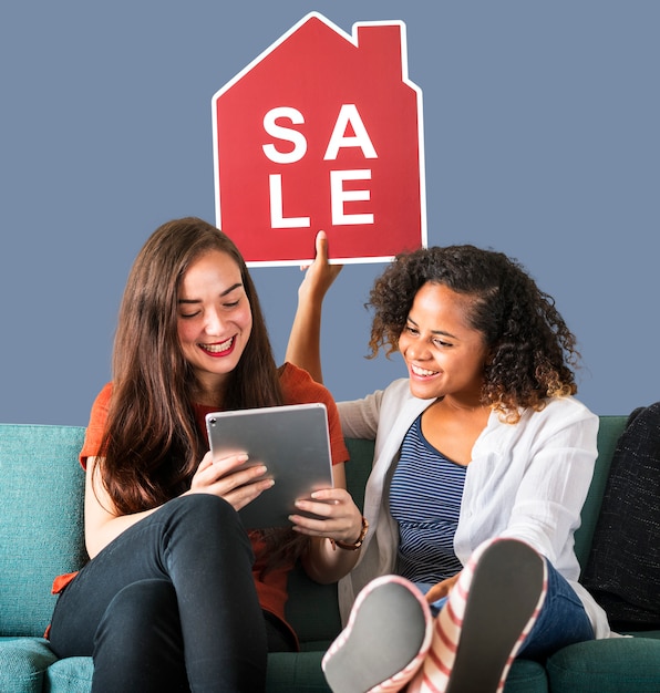 Femmes tenant une icône de vente de maison et en utilisant une tablette