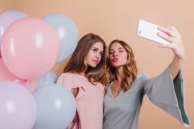 Femmes timides avec rouge à lèvres rose posant avec des ballons de fête