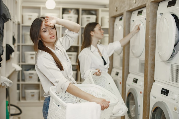 Les femmes utilisant une machine à laver font la lessive. Jeunes filles prêtes à laver les vêtements. Intérieur, concept de processus de lavage