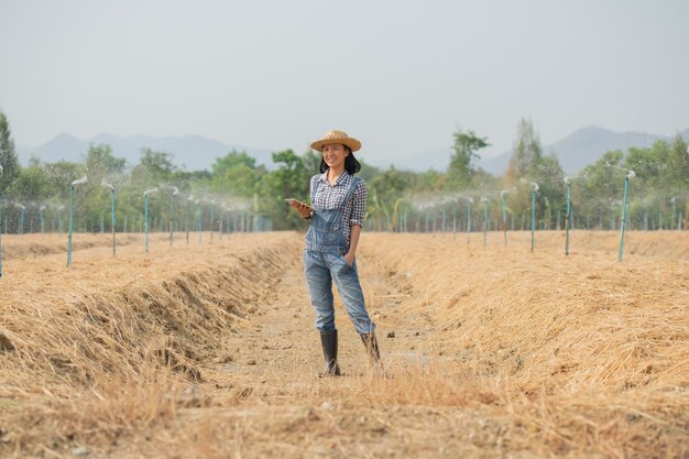 Ferme intelligente. Belle agricultrice utilise une tablette pour contrôler sa ferme et son entreprise avec bonheur et sourire. Concept d'entreprise et d'agriculture. Un agriculteur ou un agronome examine préparer une parcelle pour la culture de légumes.