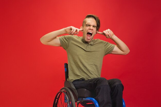 Fermer les oreilles. Portrait d'un jeune homme handicapé caucasien sur rouge