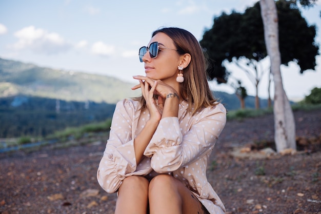 Fermer le portrait de jeune femme avec des lunettes de soleil et des boucles d'oreilles au coucher du soleil chaud dans le parc