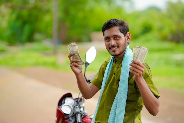 Fermier indien assis sur son nouveau vélo et montrant de l'argent.