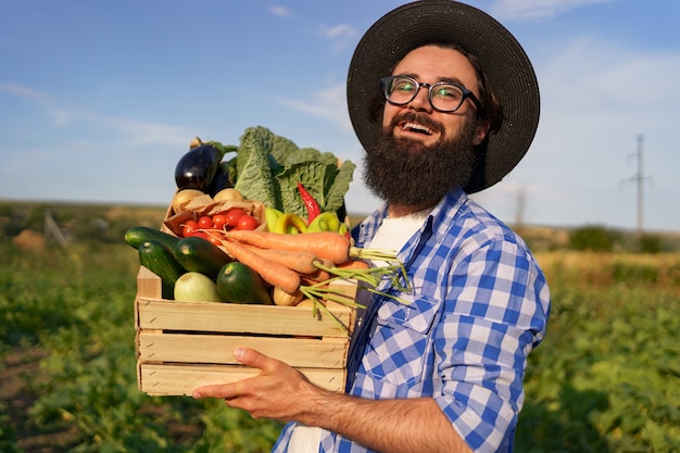 Photo gratuite le fermier tient une boîte en bois avec des légumes frais en entrant dans son jardin. se préparer à la livraison écologique biologique