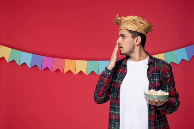 Festa junina heureux mec mignon portant un chapeau de paille célébrant le festival brésilien tenant du pop-corn