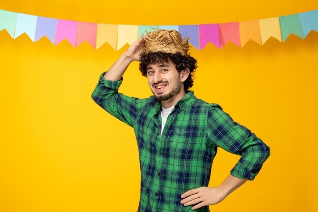 Festa junina jeune mec mignon en chapeau de paille et festival brésilien de drapeaux colorés avec la main sur la taille