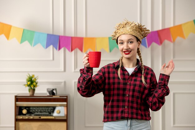 Festa junina jolie fille au chapeau de paille au milieu de l'été brésilien avec des drapeaux colorés radio rétro et une tasse rouge