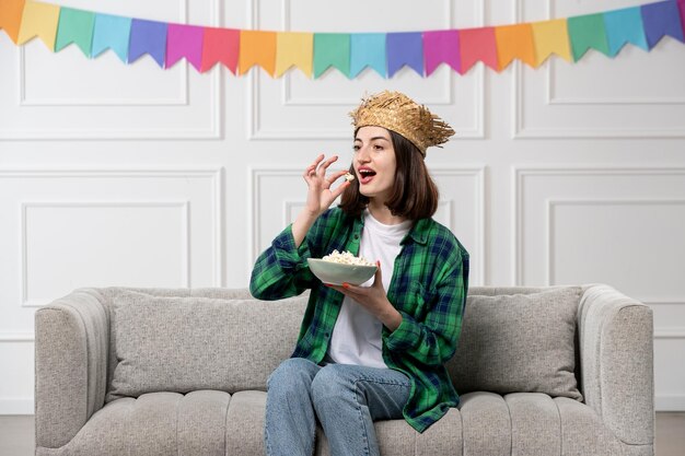 Festa junina jolie jolie fille en chemise verte chapeau de paille avec des drapeaux colorés mangeant du pop-corn