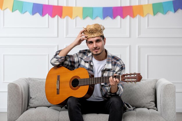 Festa junina mignon beau mec en chemise à carreaux en chapeau de paille célébrant le festival jouant à la guitare