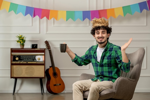 Festa junina mignon jeune homme au chapeau de paille avec radio rétro et drapeaux colorés tenant une tasse de café