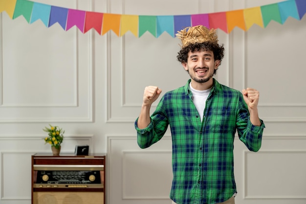 Photo gratuite festa junina mignon jeune mec en chapeau de paille avec radio rétro et drapeaux colorés excité avec les poings levés