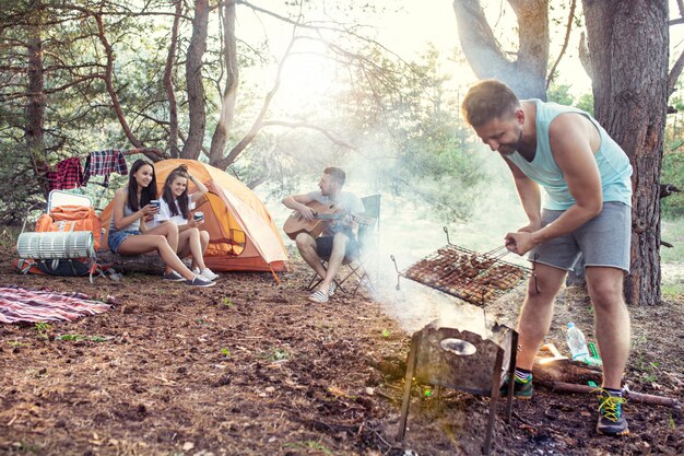 Fête, camping de groupe d'hommes et de femmes en forêt. Ils se détendent, chantent une chanson et cuisinent un barbecue