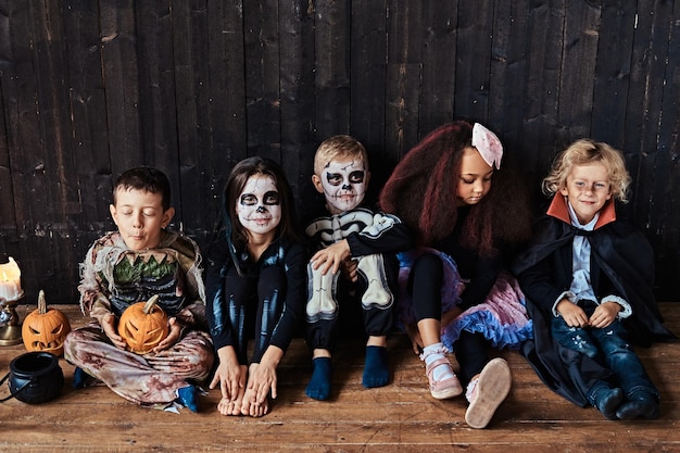 Fête d'Halloween avec des enfants de groupe assis ensemble sur un plancher en bois dans une vieille maison.