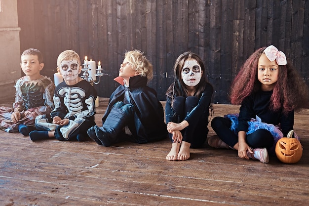 Photo gratuite fête d'halloween avec des enfants de groupe assis ensemble sur un plancher en bois dans une vieille maison.