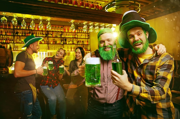 Fête de la Saint Patrick. Des amis heureux célèbrent et boivent de la bière verte. Jeunes hommes et femmes portant un chapeau vert. Intérieur du pub.