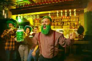 Photo gratuite fête de la saint patrick. des amis heureux célèbrent et boivent de la bière verte. jeunes hommes et femmes portant un chapeau vert. intérieur du pub.