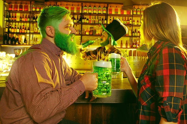 Fête de la Saint Patrick. Des amis heureux célèbrent et boivent de la bière verte. Jeunes hommes et femmes portant des chapeaux verts. Intérieur du pub.
